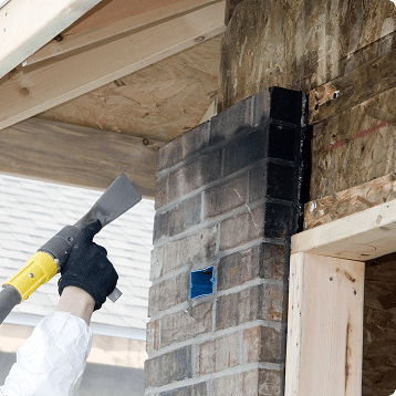 Technician scraping fire-damaged brick and wall framing during restoration work